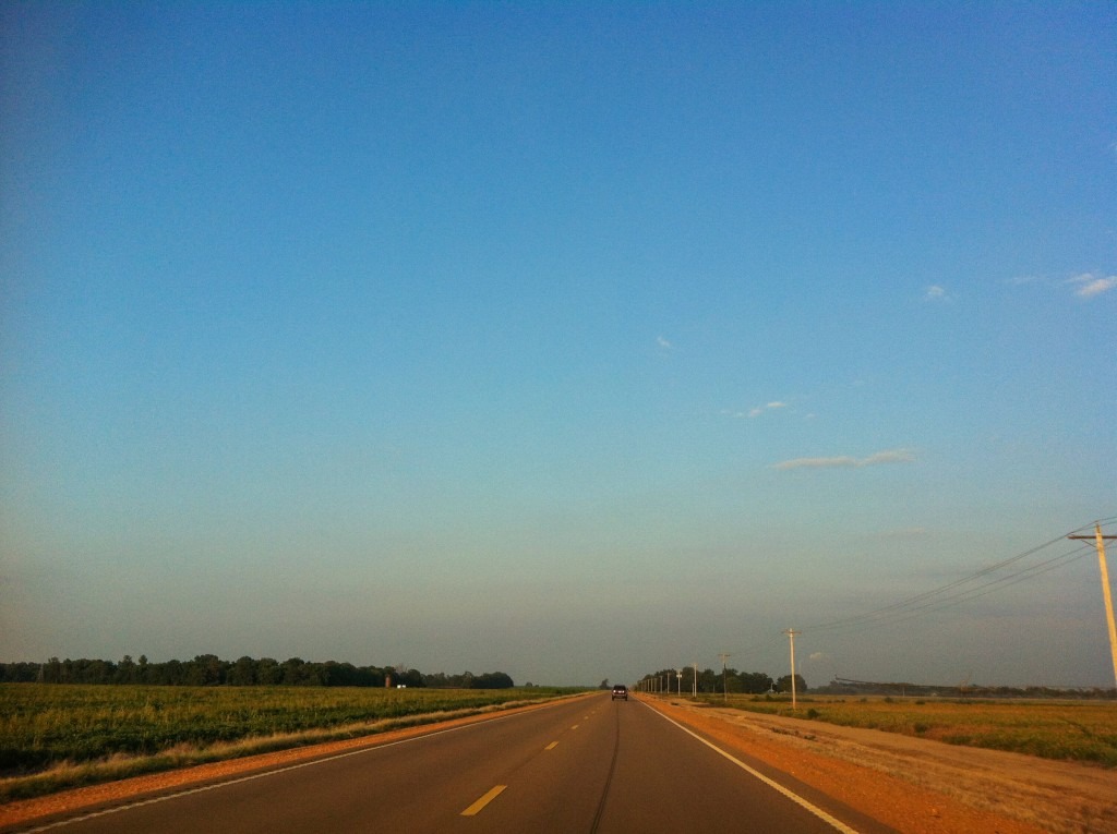 A photo is shown of a two-lane road running toward the horizon of the flat land of the Mississippi Delta. The sky glows in many shades of blue.