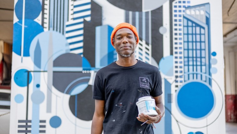 A man holds a paint can while standing in front of a painted backdrop.