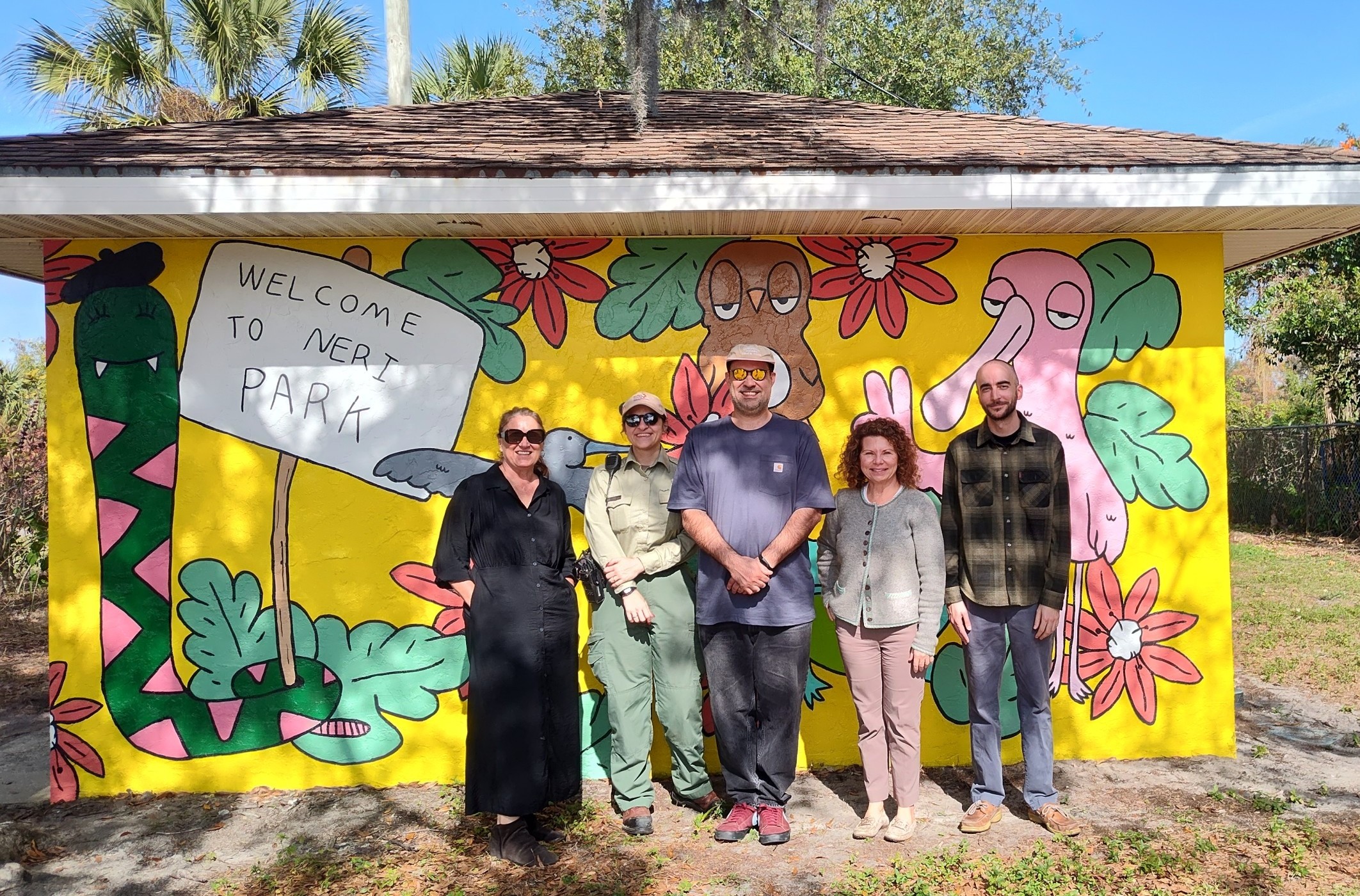 A group of people pose in front of a mural.